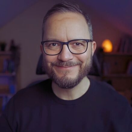 Man with glasses smiling indoors.